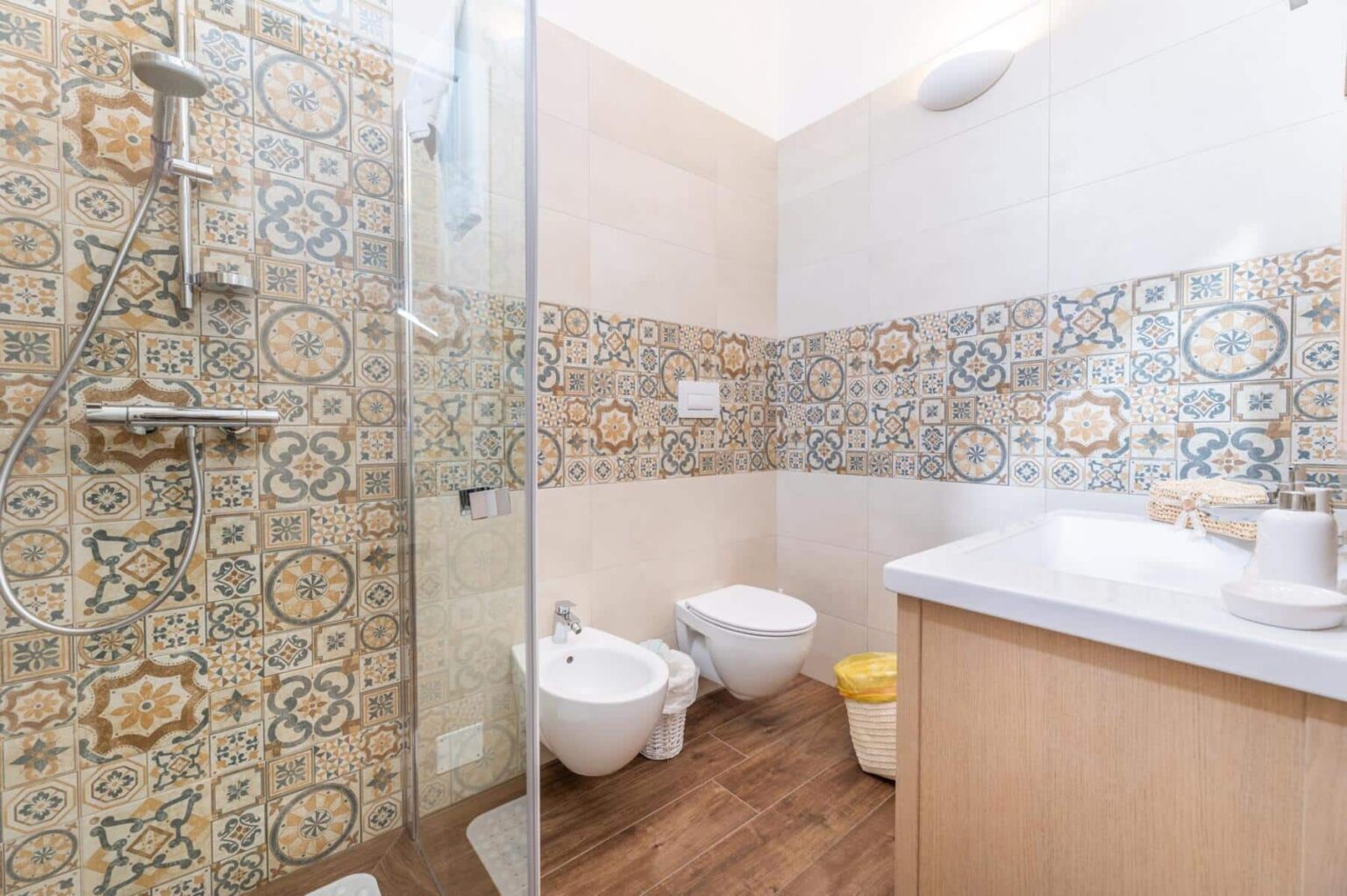 Modern bathroom featuring a glass shower, decorative tiled walls, a sleek vanity with a sink, and a bidet, providing a stylish and functional space. | Only on SopranoVillas
