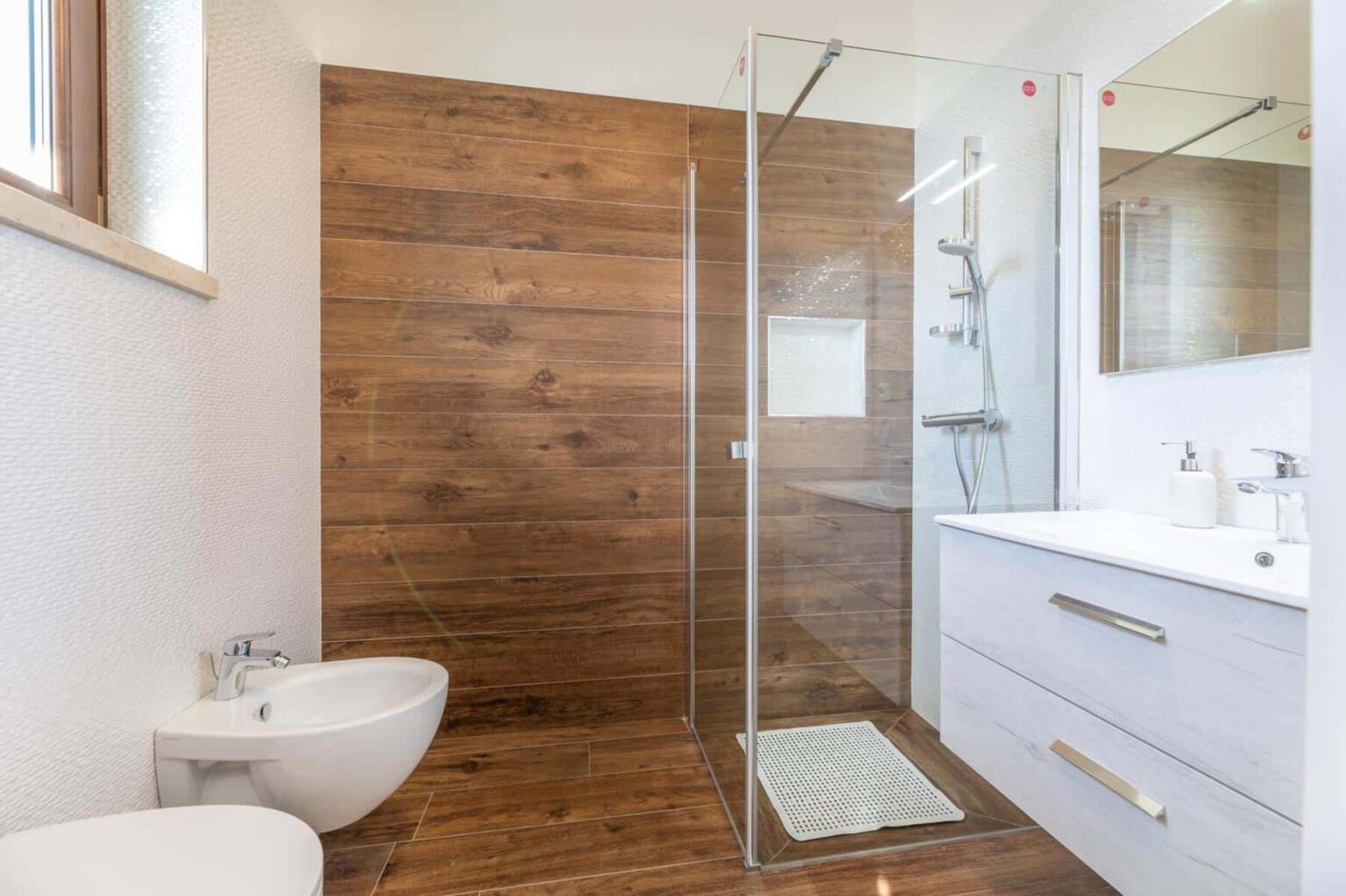Modern bathroom featuring a glass shower enclosure, wooden accent wall, sleek white vanity, and minimalist decor, ideal for contemporary home design. | Only on SopranoVillas