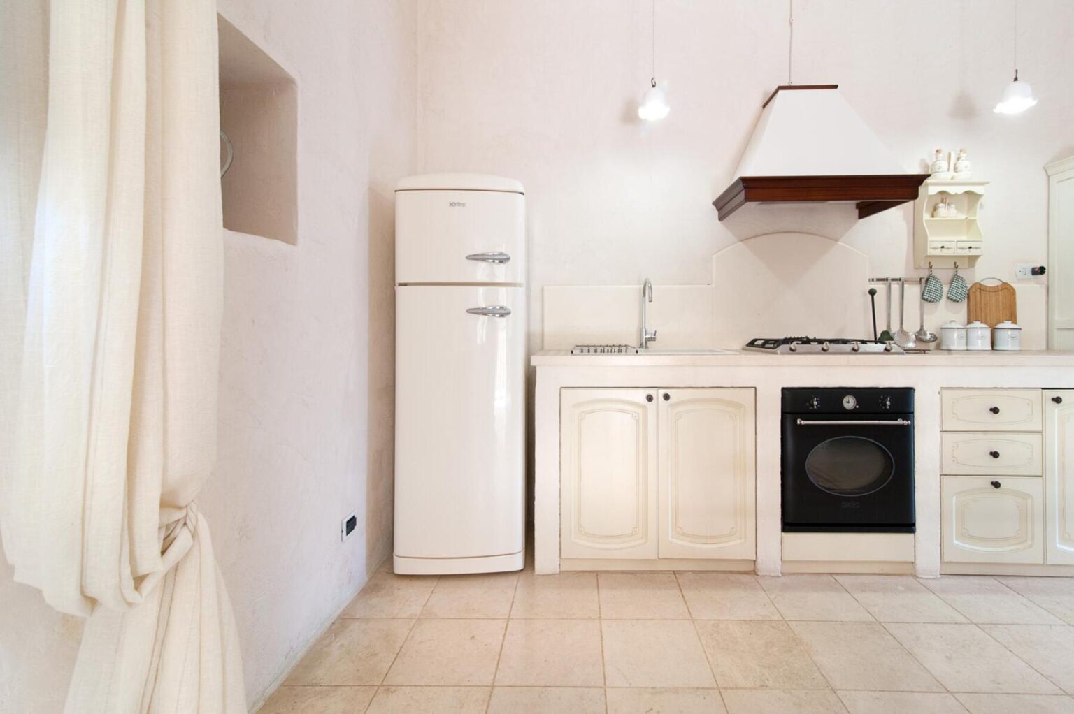Modern kitchen interior featuring a white refrigerator, black stove, and minimalist design elements. The space is well-lit with pendant lighting and has a clean, contemporary aesthetic. | Only on SopranoVillas