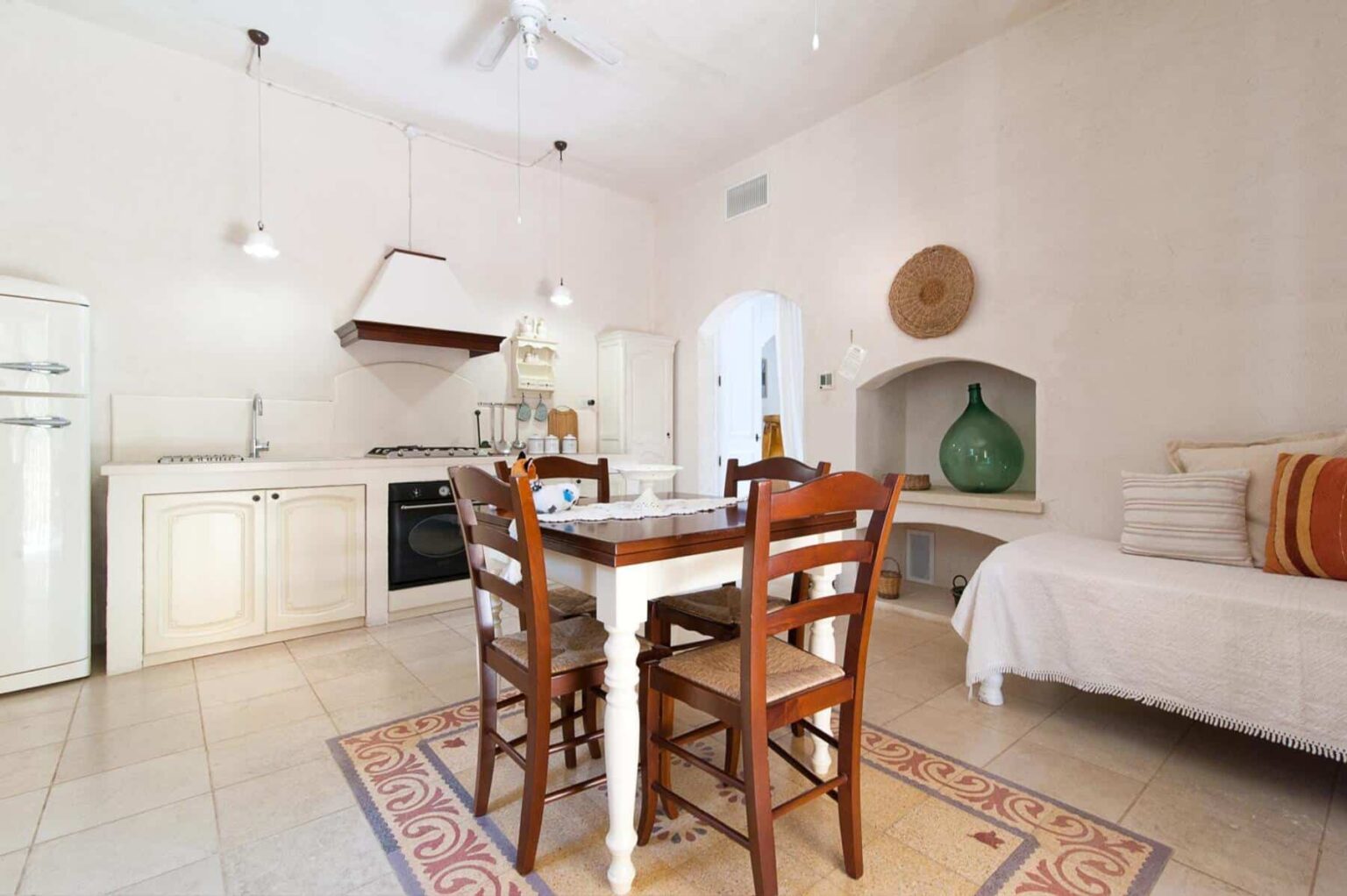 Bright and airy kitchen and dining area featuring a wooden table with chairs, a cozy daybed, modern appliances, and decorative accents in a minimalist style. | Only on SopranoVillas