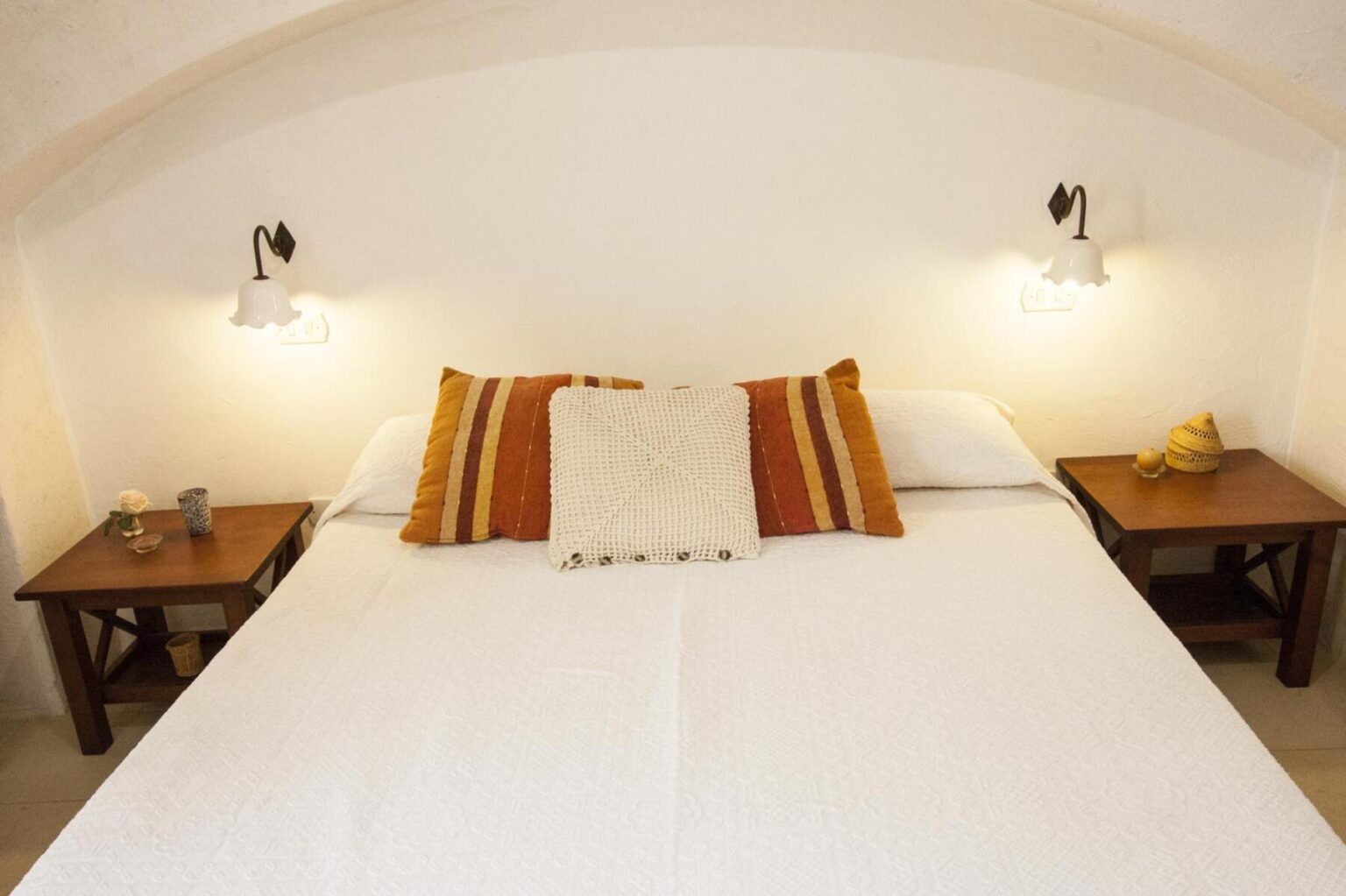Cozy bedroom featuring a large white bed with decorative pillows, two wooden bedside tables, and stylish wall sconces, creating a warm and inviting atmosphere. | Only on SopranoVillas