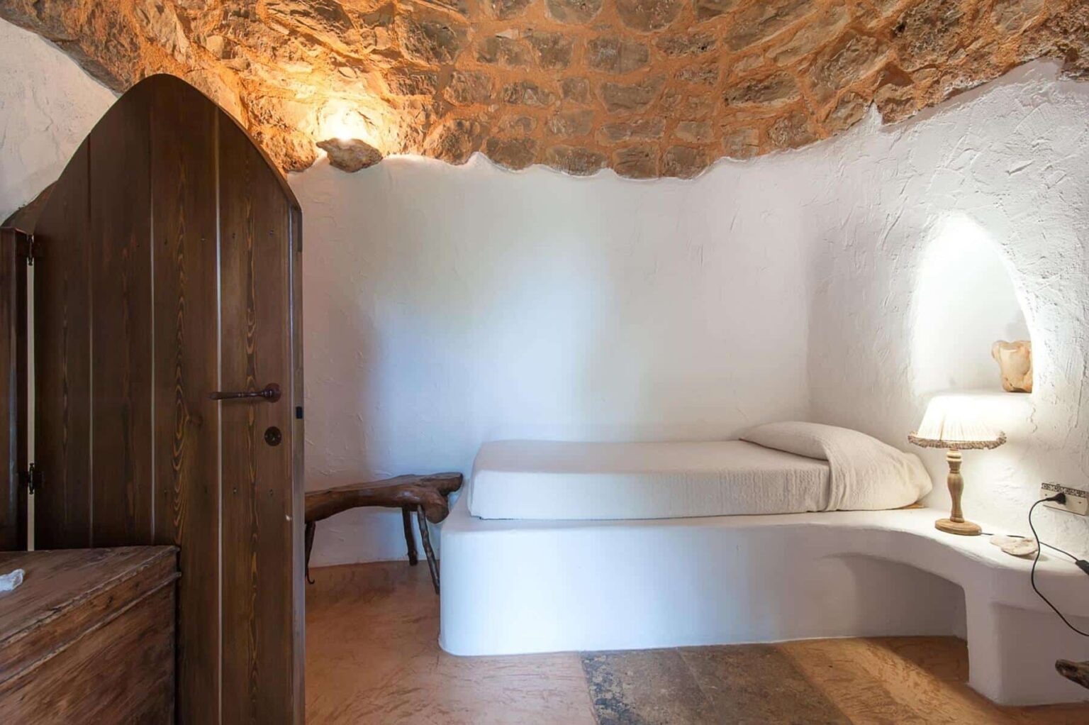 Cozy interior of a minimalist bedroom featuring a stone ceiling, a simple bed, wooden furniture, and soft lighting, ideal for a tranquil retreat. | Only on SopranoVillas