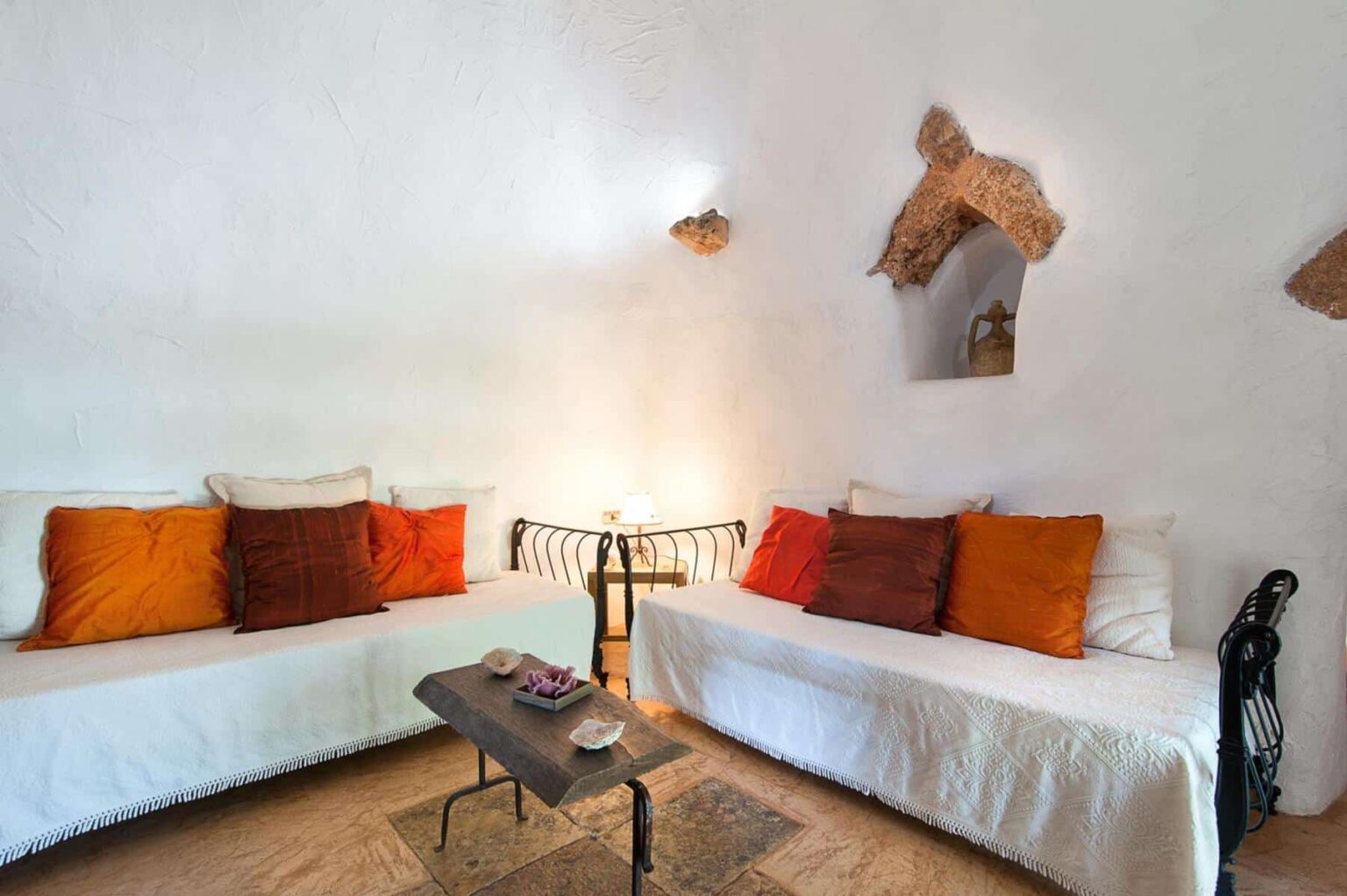 Cozy living room with two white sofas adorned with colorful cushions, a wooden coffee table, and decorative wall features, creating a warm and inviting atmosphere. | Only on SopranoVillas