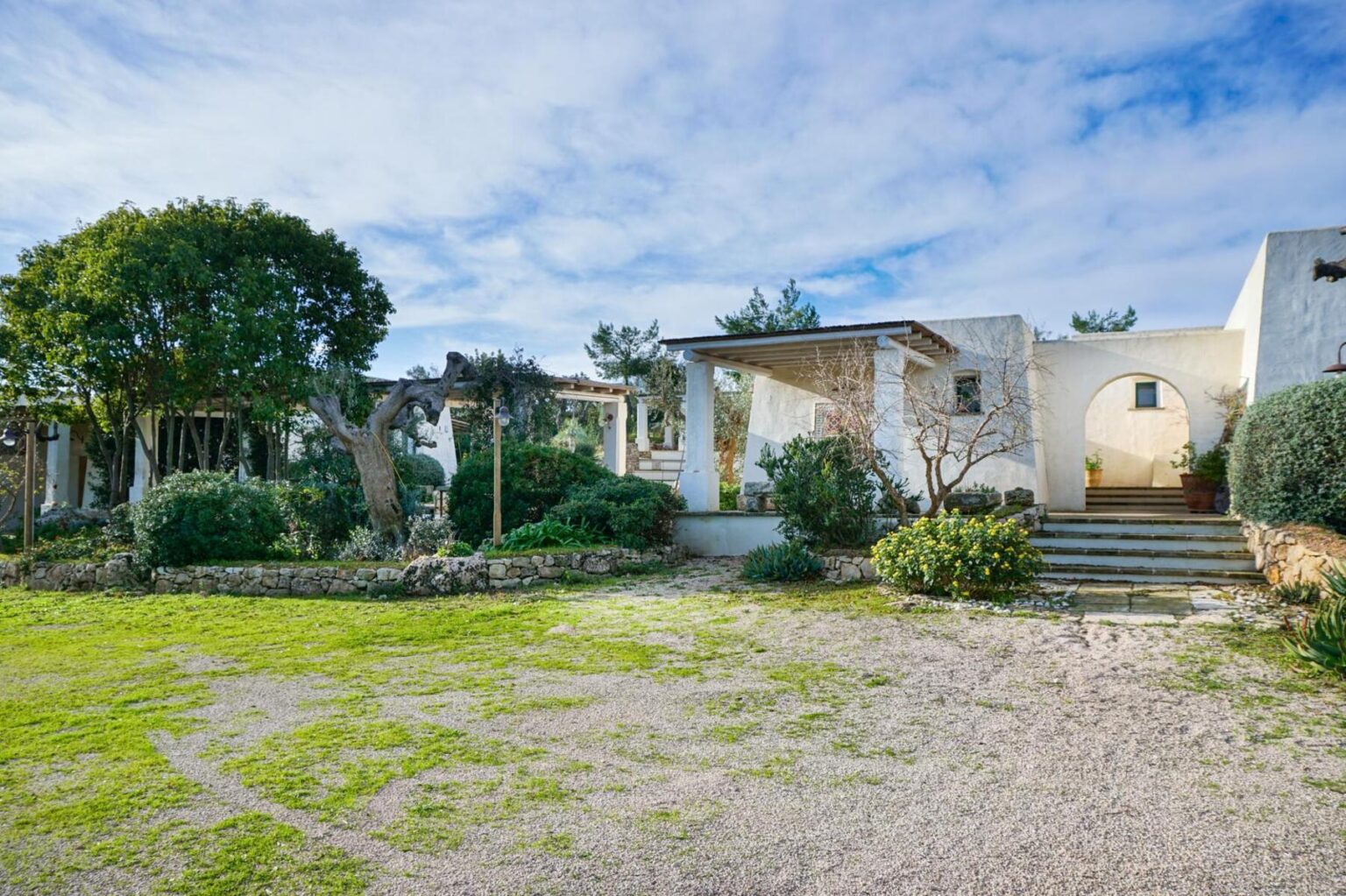 Modern architectural home surrounded by lush greenery and a well-maintained garden, featuring a gravel pathway leading to the entrance under a clear blue sky. | Only on SopranoVillas