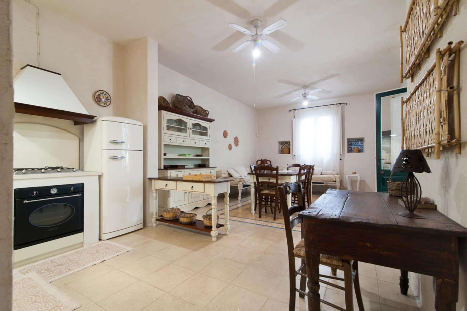 Bright and airy kitchen and dining area featuring a vintage stove, modern refrigerator, wooden dining table, and comfortable seating, complemented by natural light from large windows and tastefully decorated with wall art. | Only on SopranoVillas
