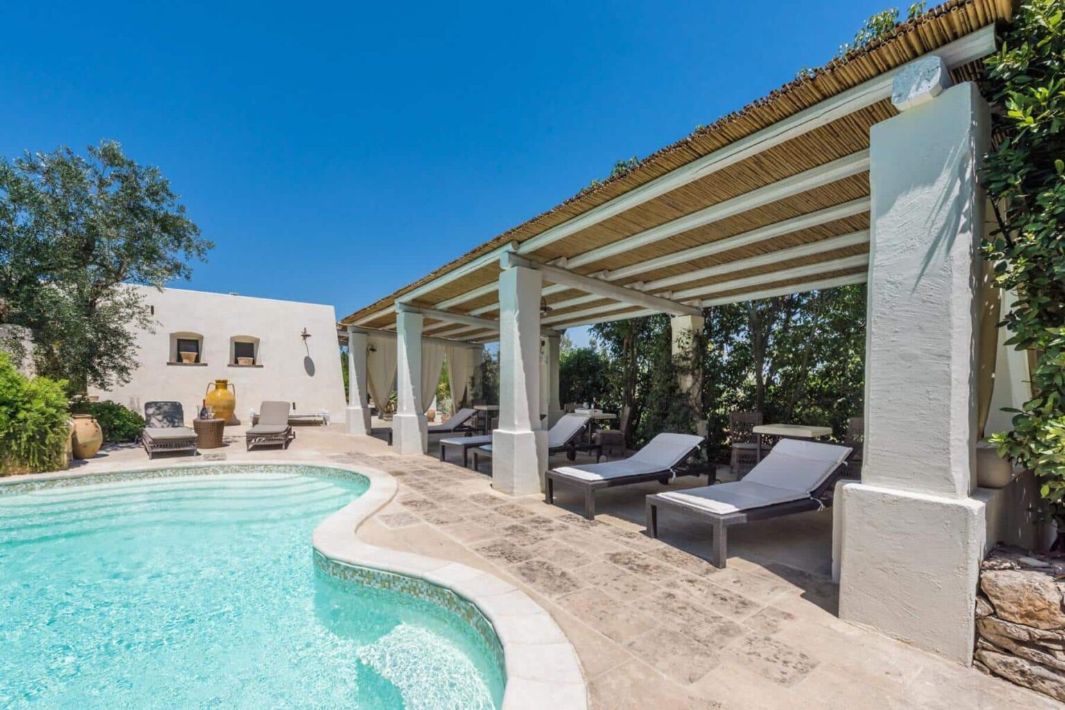 Luxury villa with a pool and shaded lounging area, surrounded by greenery and clear blue skies, perfect for relaxation and outdoor living. | Only on SopranoVillas