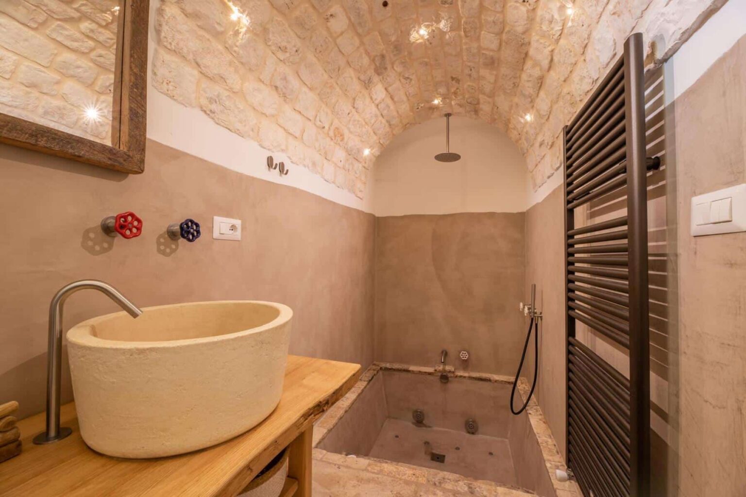 Modern bathroom featuring a stone arch ceiling, minimalist design, and natural materials. The image showcases a unique stone sink, stylish wall-mounted faucets, a spacious bathtub, and a heated towel rack, highlighting a blend of functionality and aesthetic appeal. | Only on SopranoVillas