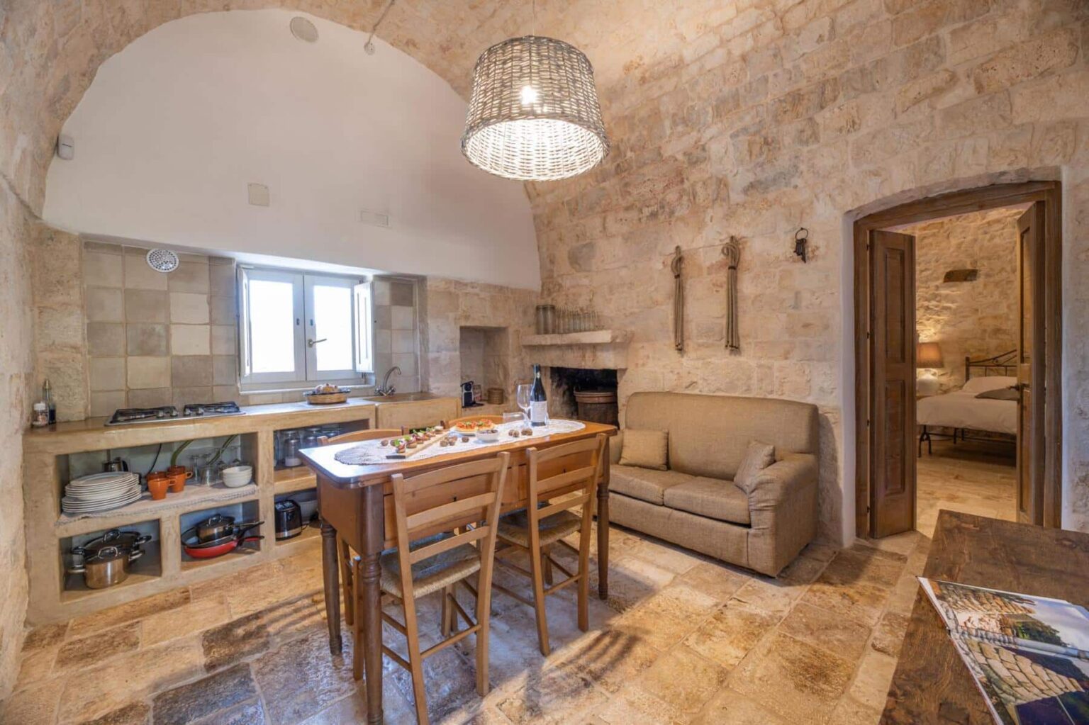 Cozy kitchen and dining area featuring stone walls, a wooden dining table with chairs, a comfortable sofa, and a rustic light fixture, creating a warm and inviting atmosphere. Natural light streams in through the windows, enhancing the charming decor. | Only on SopranoVillas
