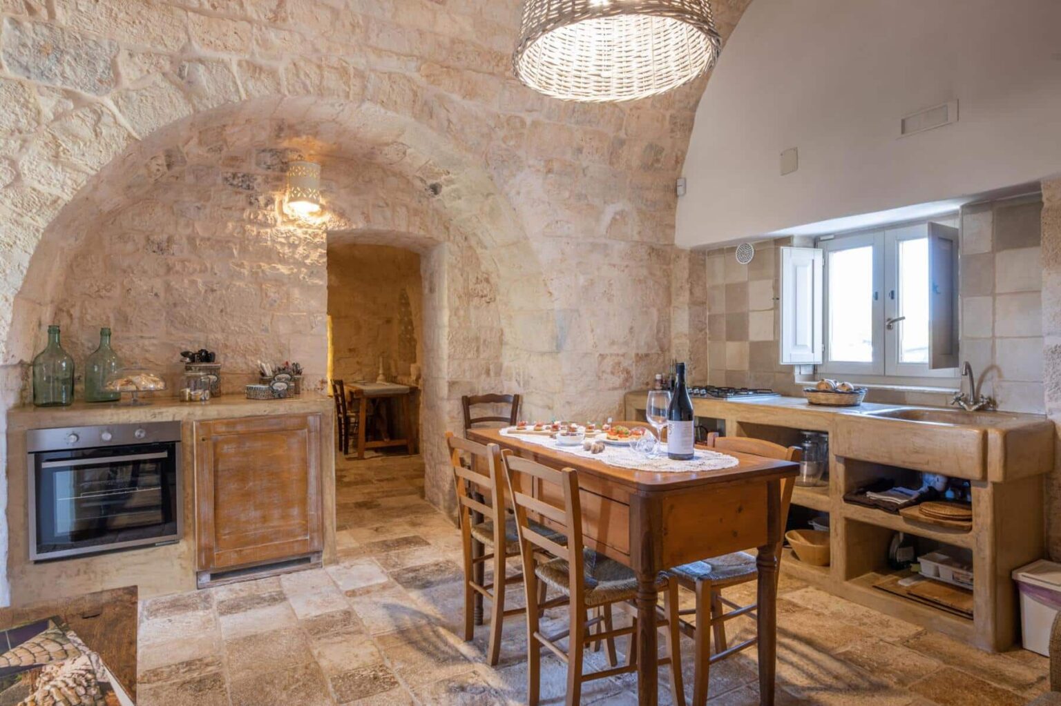 Rustic kitchen interior featuring stone walls, a wooden dining table with chairs, modern appliances, and a unique chandelier, showcasing a blend of traditional and contemporary design elements. | Only on SopranoVillas