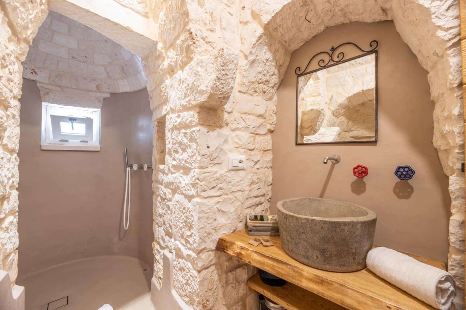 Stylish bathroom interior featuring natural stone walls, a modern shower, a concrete sink, and a wooden countertop. The design combines rustic charm with contemporary elements, including a mirror and decorative faucet handles. | Only on SopranoVillas