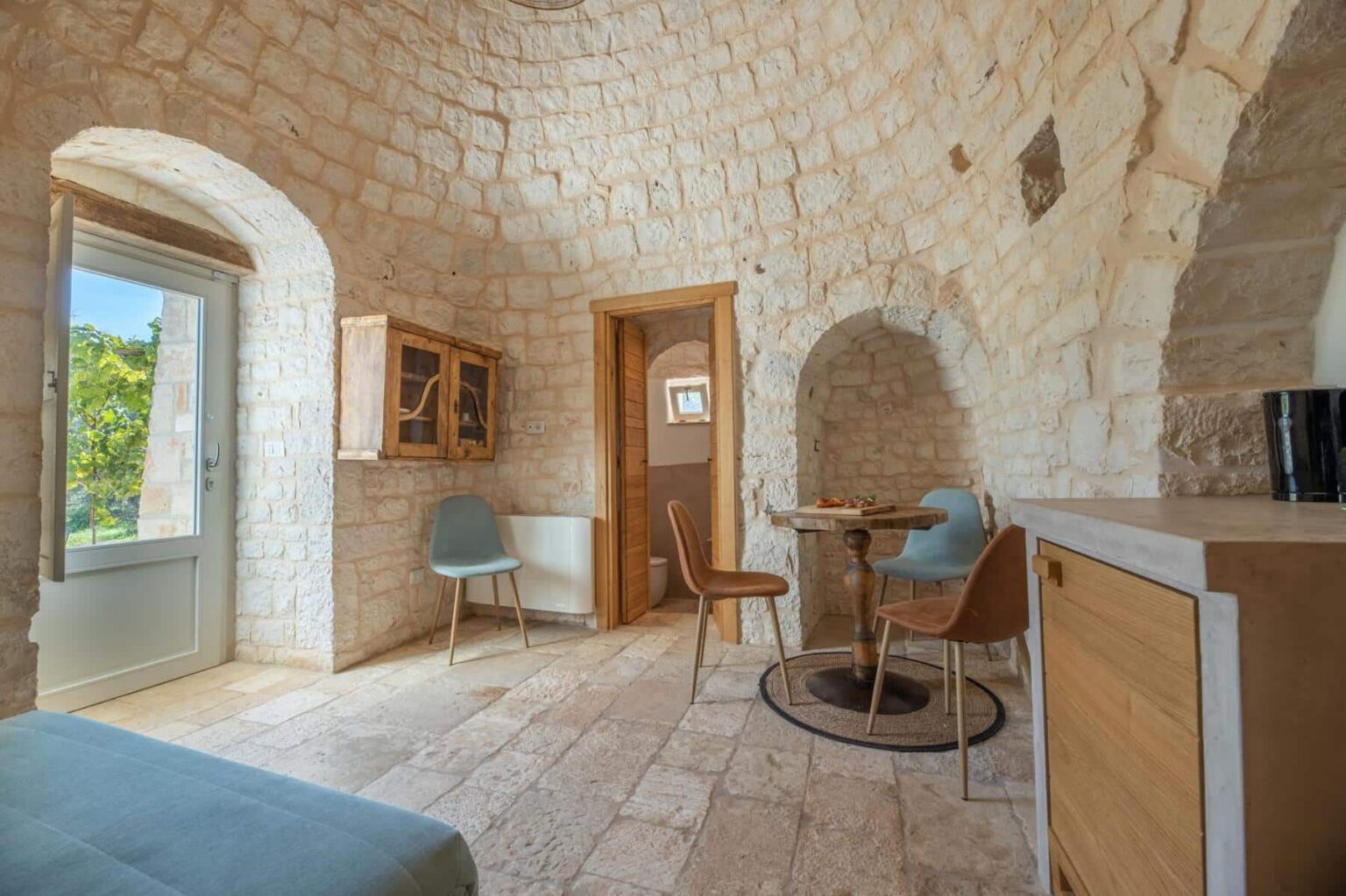Cozy interior of a stone cottage featuring a round ceiling, wooden furnishings, and a small dining area with chairs and a table, complemented by natural light from a window. | Only on SopranoVillas