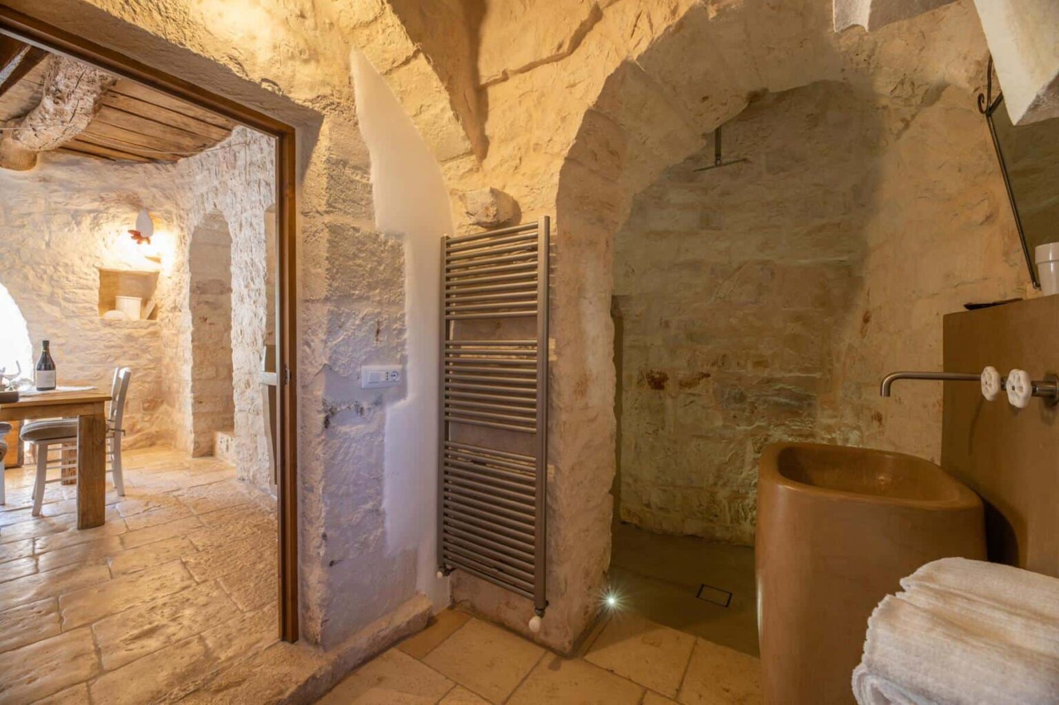 Rustic bathroom interior featuring stone walls, a modern heated towel rack, and a unique sink design. The space showcases natural materials and a warm, inviting atmosphere, ideal for a cozy retreat. | Only on SopranoVillas