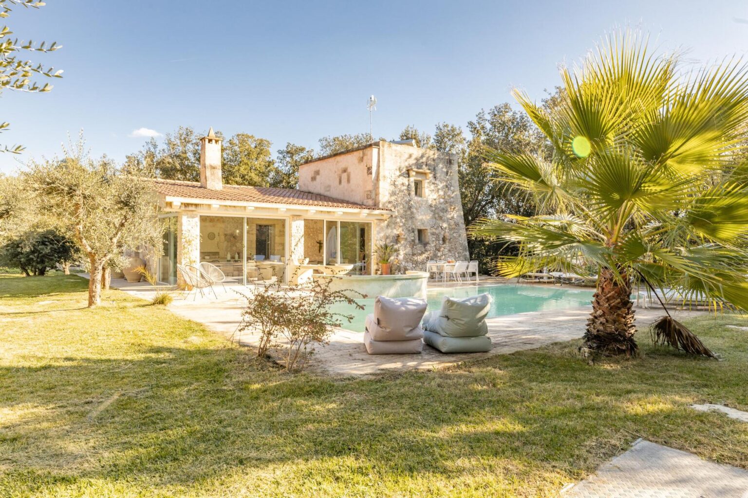Charming stone villa with a swimming pool surrounded by greenery and palm trees, perfect for a relaxing getaway. | Only on SopranoVillas