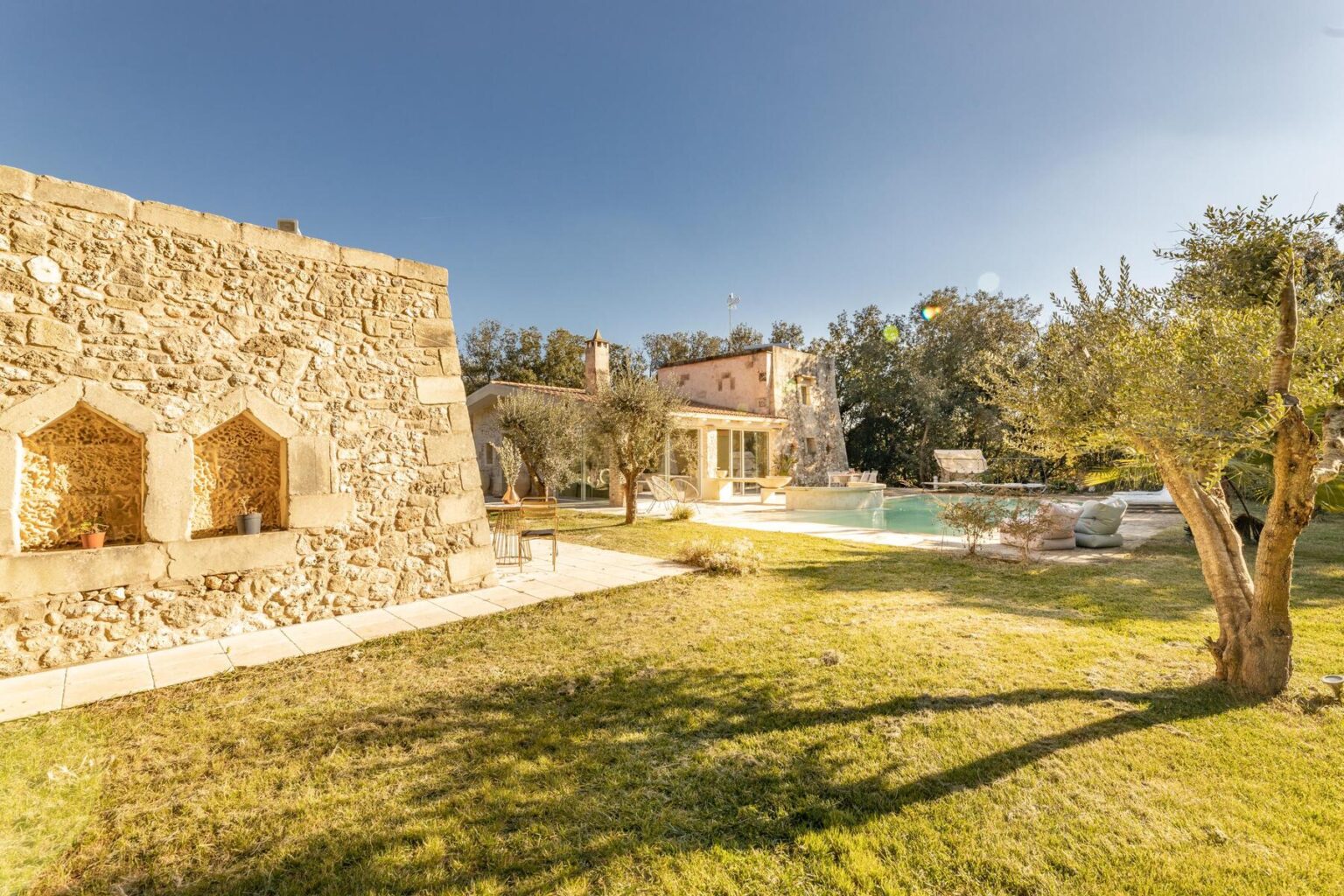 Stone villa with a lush green lawn and swimming pool, surrounded by olive trees under a clear blue sky. Ideal for a tranquil getaway or vacation rental. | Only on SopranoVillas