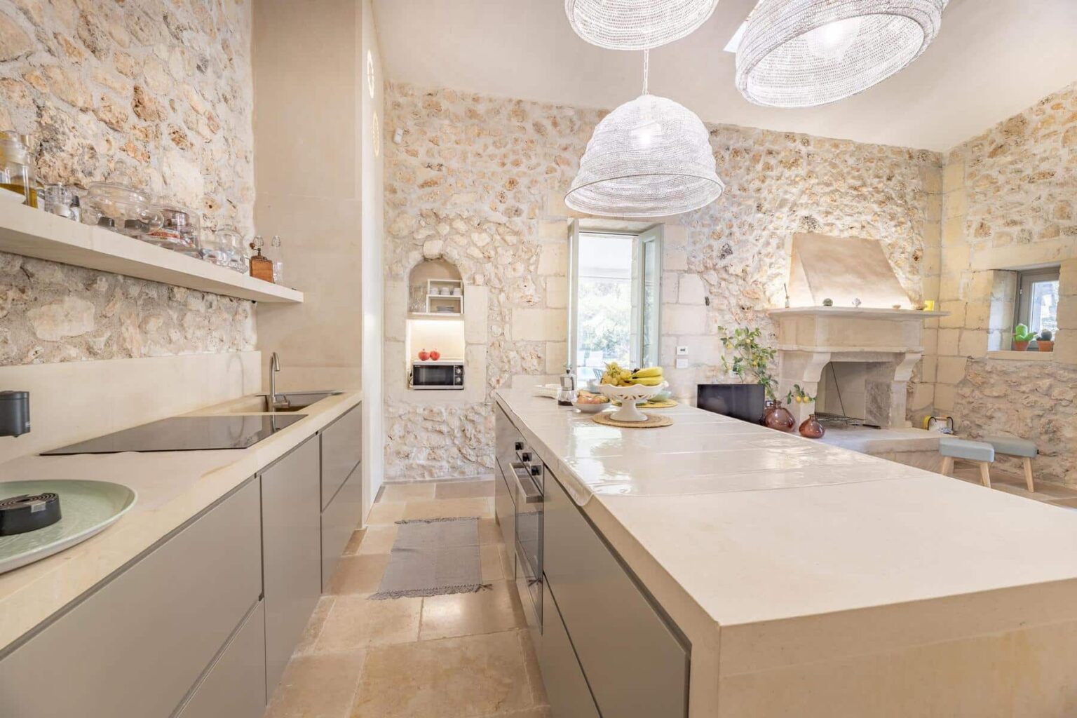 Modern kitchen featuring a spacious island with a sleek countertop, stone walls, and stylish pendant lighting, creating a bright and inviting atmosphere. | Only on SopranoVillas