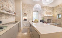 Modern kitchen featuring a spacious island with a sleek countertop, stone walls, and stylish pendant lighting, creating a bright and inviting atmosphere.