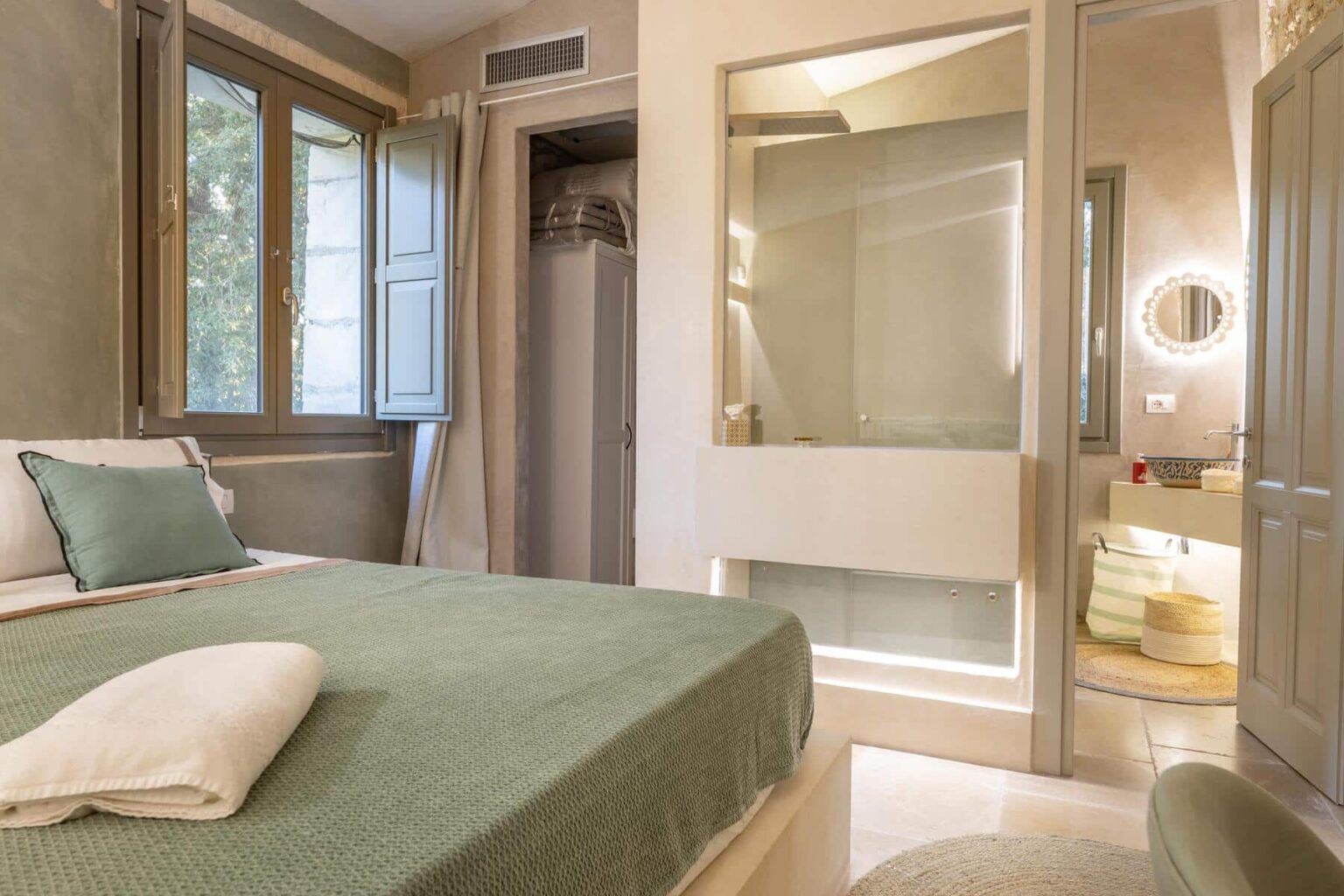 Cozy bedroom featuring a green bedspread, large windows with natural light, and a modern bathroom with glass enclosure. The interior design combines elegance and comfort, ideal for relaxation. | Only on SopranoVillas