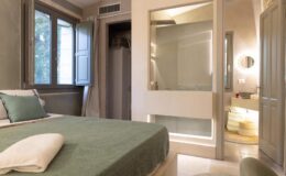 Modern bedroom interior featuring a green bedspread, natural light from large windows, and a stylish en-suite bathroom. The decor combines minimalism with comfort, ideal for a relaxing stay.