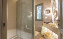 Modern bathroom featuring a glass shower enclosure, illuminated mirrors, and stylish decor. The design highlights neutral tones and elegant storage solutions, creating a serene and functional space.