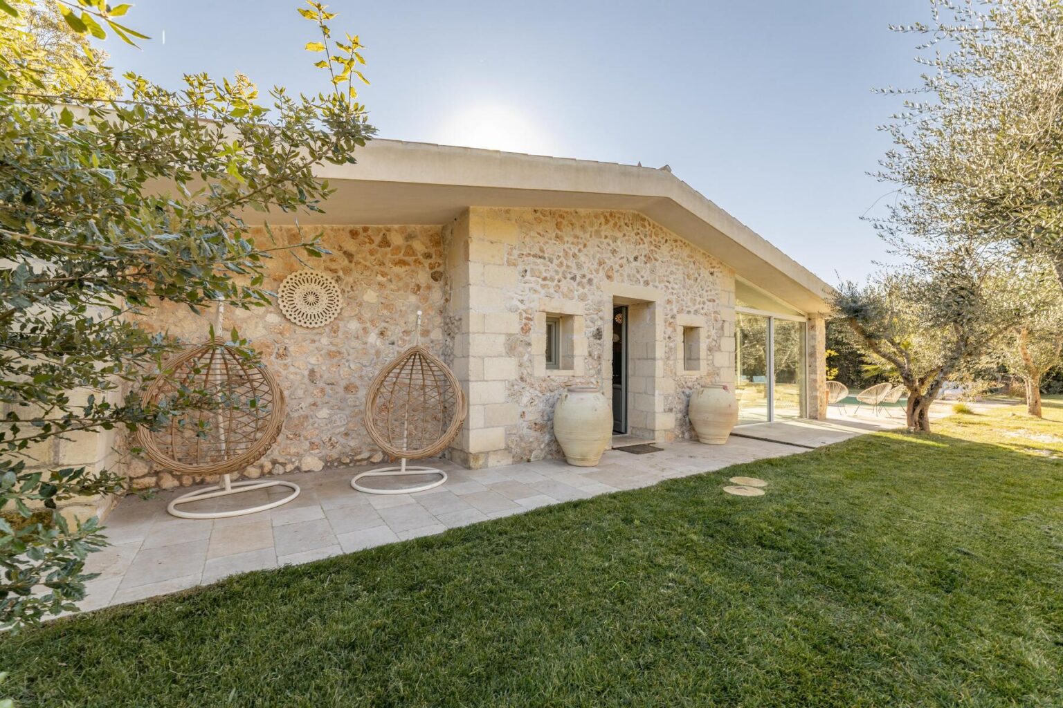 Modern stone house with a landscaped garden, featuring olive trees and decorative outdoor seating. Ideal for relaxation and outdoor living. | Only on SopranoVillas