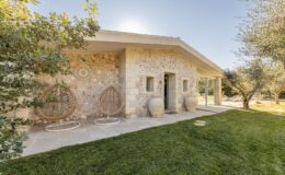 Modern stone house with a landscaped garden, featuring olive trees and decorative outdoor seating. Ideal for relaxation and outdoor living.