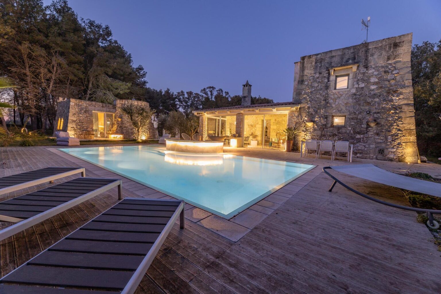 Luxury villa with a stunning pool area illuminated at dusk, surrounded by stone walls and lush trees, perfect for relaxation and outdoor gatherings. | Only on SopranoVillas