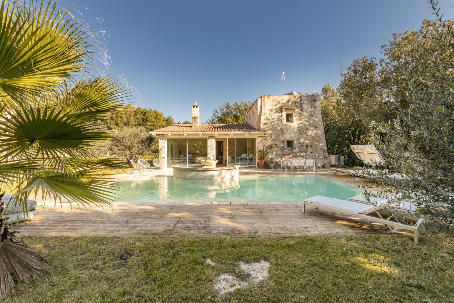 Charming stone villa with a swimming pool surrounded by lush greenery and palm trees, featuring a sun terrace and modern outdoor seating, ideal for relaxation and leisure. | Only on SopranoVillas