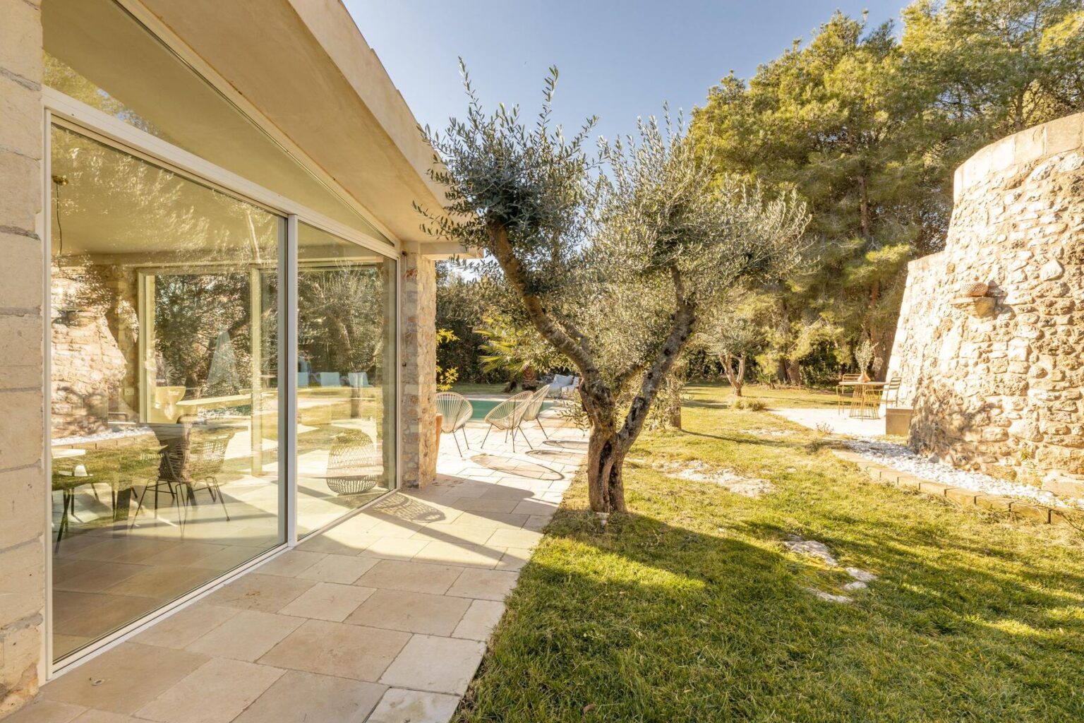 Modern villa exterior with large glass windows, olive trees, and a landscaped garden, showcasing a serene outdoor living space. | Only on SopranoVillas