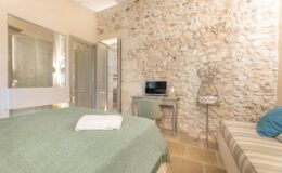 Cozy bedroom featuring a stone accent wall, a comfortable green bedspread, a small desk with a TV, and a stylish mannequin display. Ideal for relaxation and modern decor.