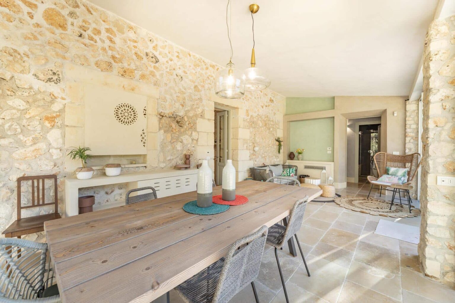 Rustic dining area featuring a large wooden table, stone walls, and modern decor. The space is bright and airy, with stylish lighting fixtures and comfortable seating arrangements. | Only on SopranoVillas