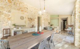 Rustic dining area featuring a large wooden table, stone walls, and modern decor. The space is bright and airy, with stylish lighting fixtures and comfortable seating arrangements.