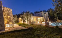 Charming villa at dusk with illuminated garden, stone architecture, and a serene swimming pool surrounded by olive trees. Ideal for a relaxing getaway.