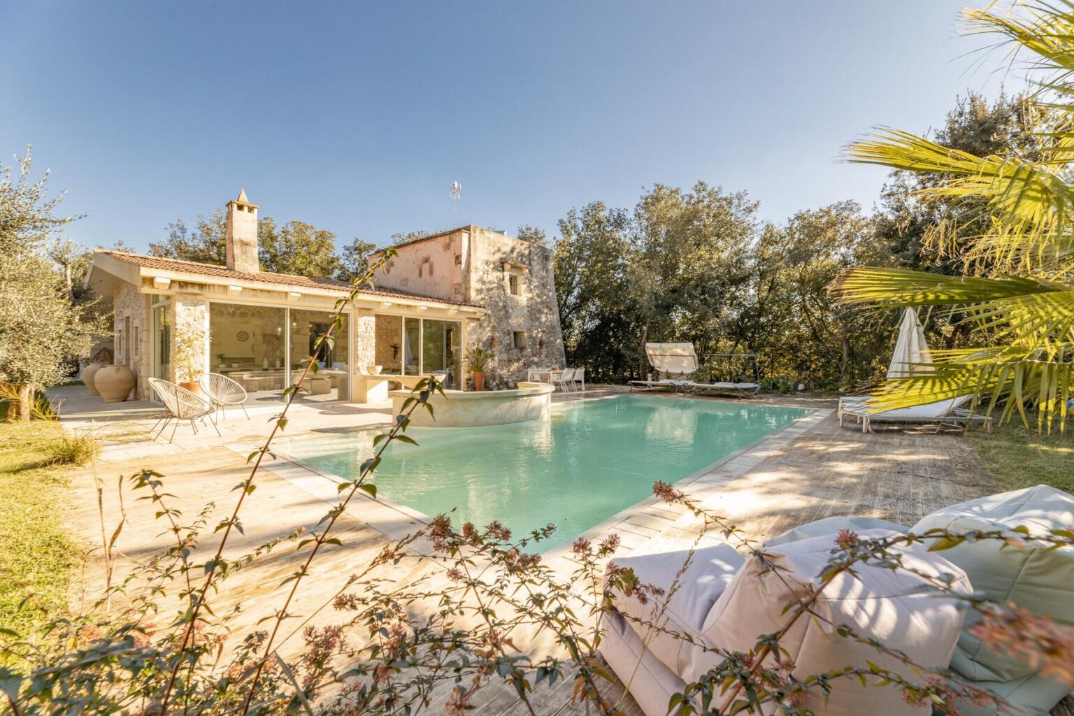 Charming stone villa with a swimming pool surrounded by lush greenery, featuring modern outdoor seating and a relaxing atmosphere, perfect for a tranquil getaway. | Only on SopranoVillas