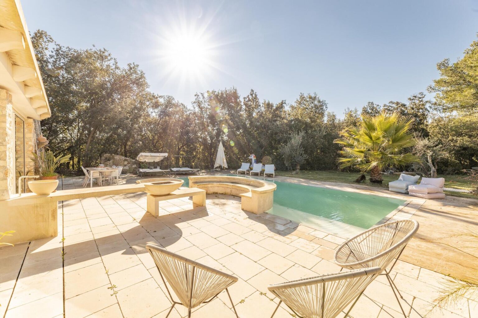 Luxury villa with a sunlit swimming pool, surrounded by lush greenery and outdoor seating, perfect for relaxation and leisure. | Only on SopranoVillas