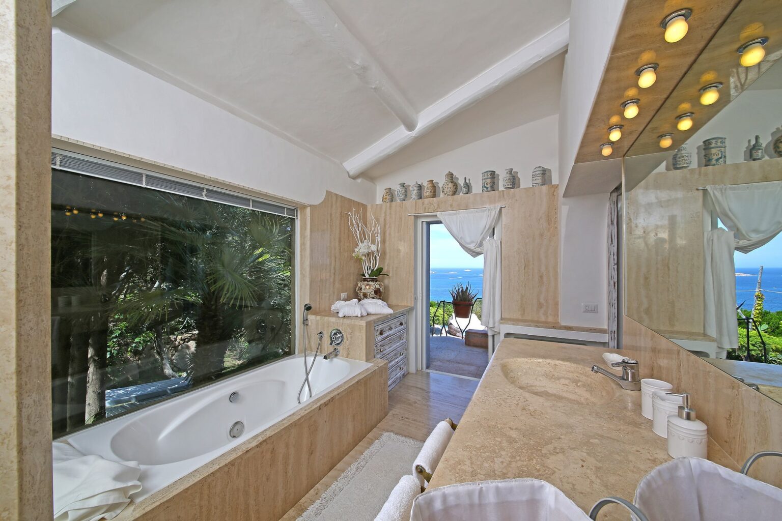 Luxurious bathroom featuring a soaking tub, large windows with ocean views, modern lighting, and elegant wooden accents, creating a serene and inviting atmosphere. | Only on SopranoVillas