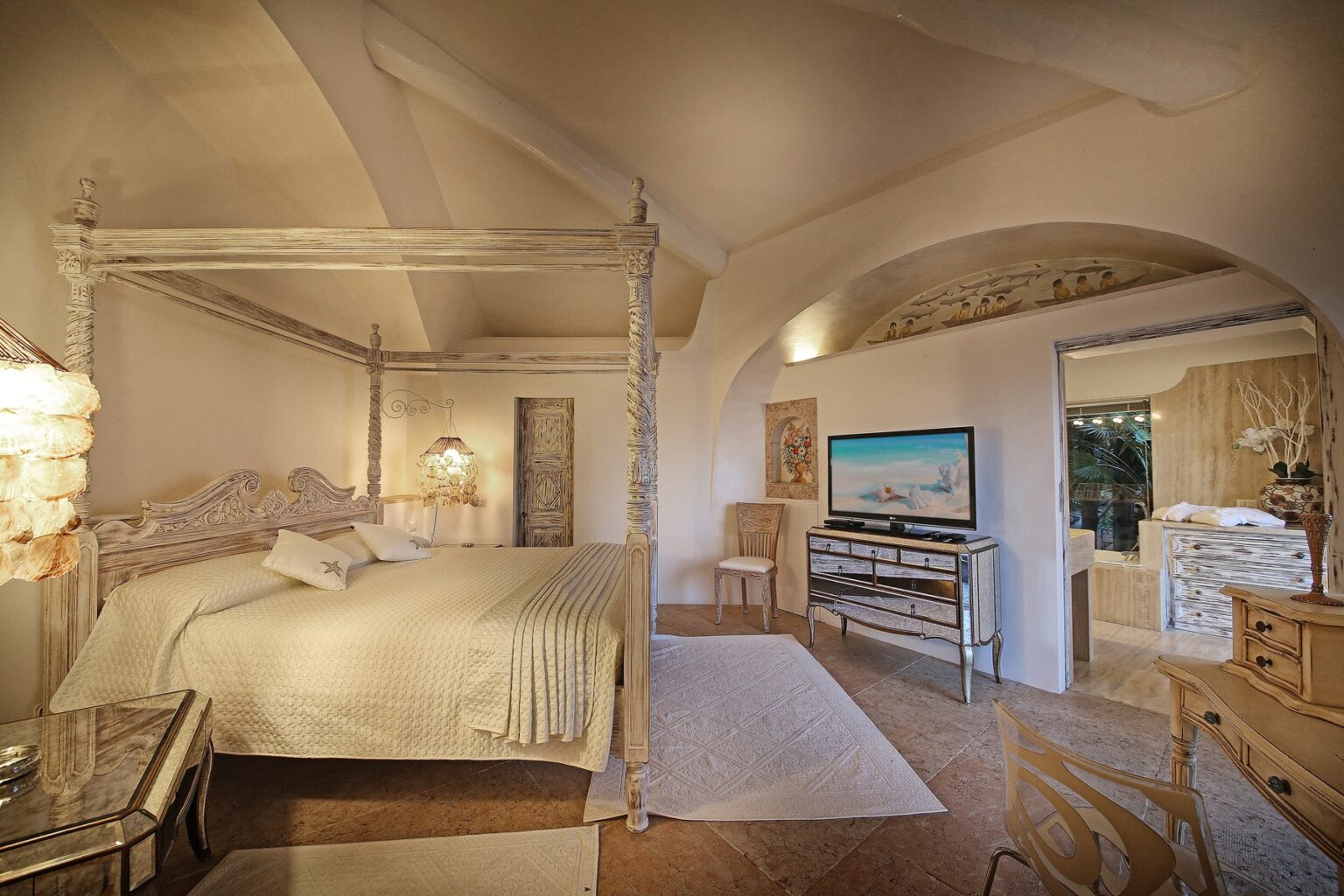 Spacious and elegant bedroom featuring a four-poster bed, soft lighting, and tasteful decor, with a television and an adjoining bathroom visible in the background. | Only on SopranoVillas