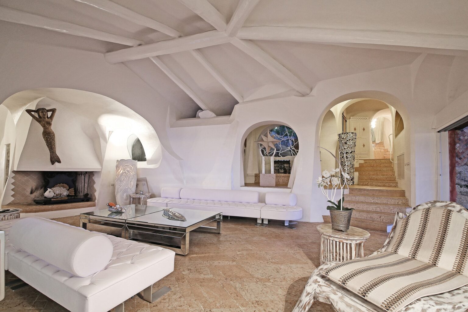 Spacious modern living room with white walls, vaulted ceiling, and elegant furnishings, featuring a cozy fireplace and arched doorways. | Only on SopranoVillas