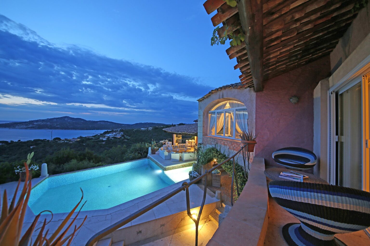Stunning sunset view from a luxury villa overlooking a serene pool and lush landscape, featuring a cozy outdoor seating area and dramatic sky. | Only on SopranoVillas