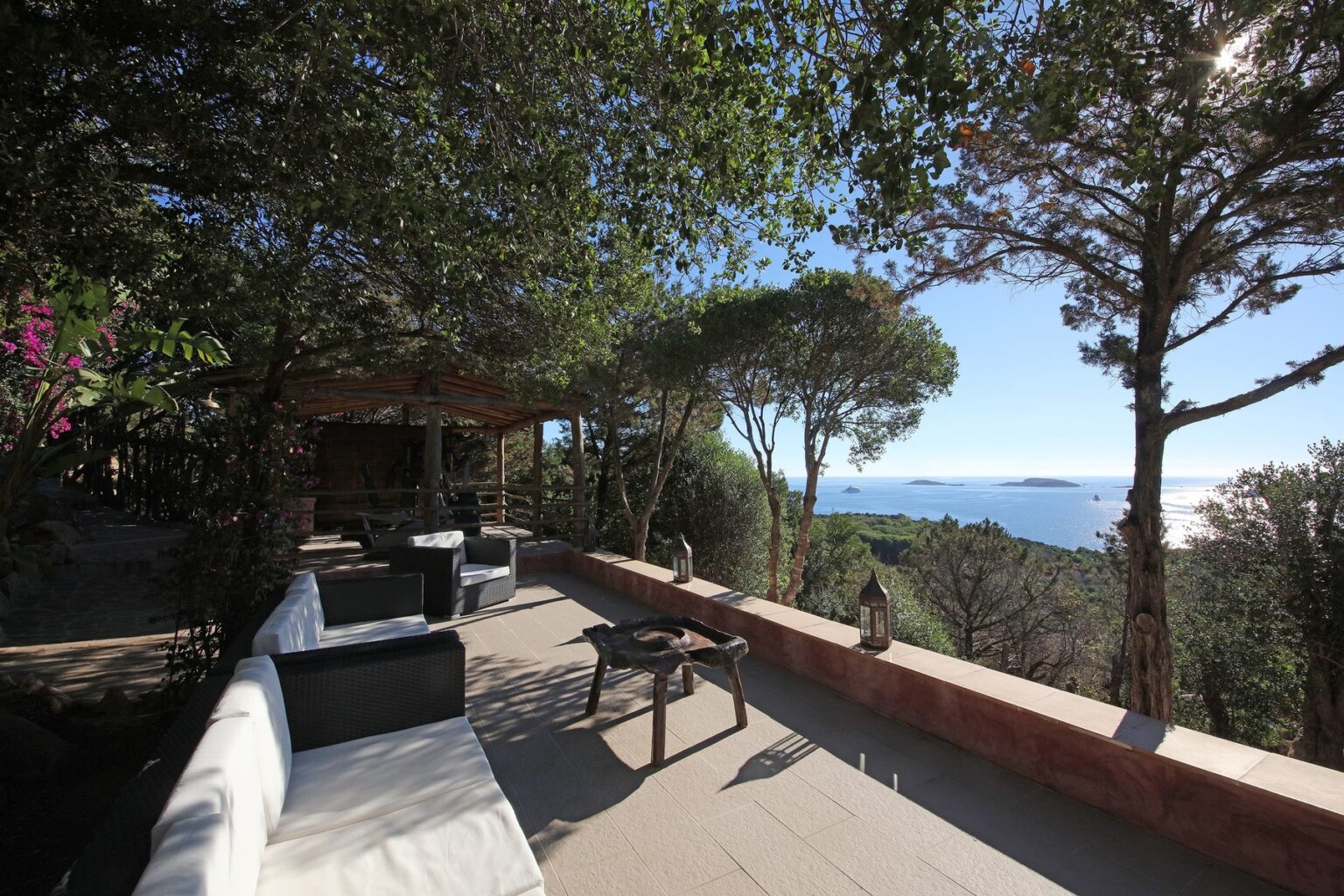 Scenic outdoor terrace with modern seating, surrounded by lush greenery and offering a stunning view of the ocean and distant islands. Ideal for relaxation and enjoying nature. | Only on SopranoVillas