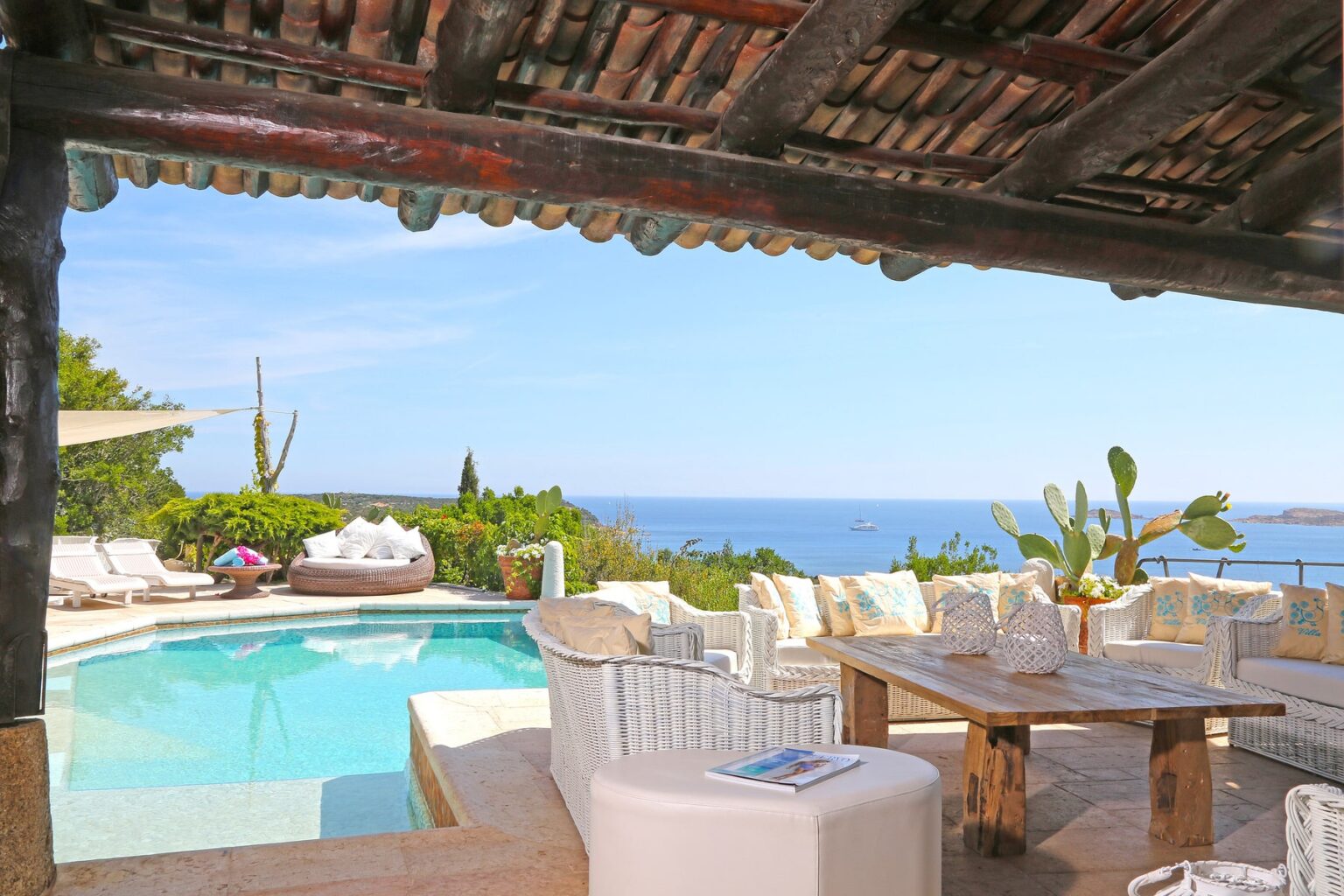 Luxurious outdoor living space featuring a stunning pool, comfortable wicker seating with decorative pillows, and a breathtaking view of the ocean. Perfect for relaxation and entertaining in a serene environment. | Only on SopranoVillas