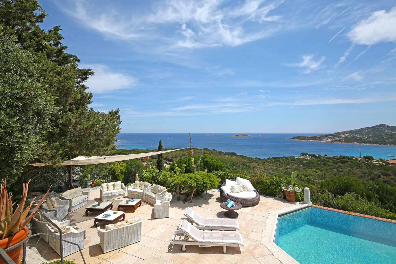 Luxurious outdoor lounge area with comfortable seating and a private pool overlooking a stunning coastal view, surrounded by lush greenery and clear blue waters. Perfect for relaxation and entertaining in a serene environment. | Only on SopranoVillas