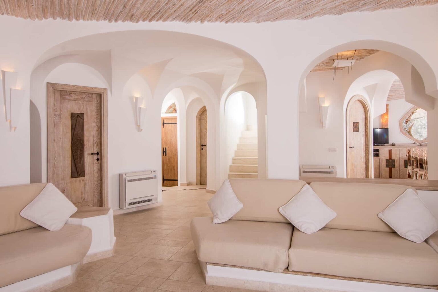 Spacious and modern interior of a stylish living room featuring arched doorways, light-colored sofas with decorative pillows, and a warm, inviting atmosphere. | Only on SopranoVillas