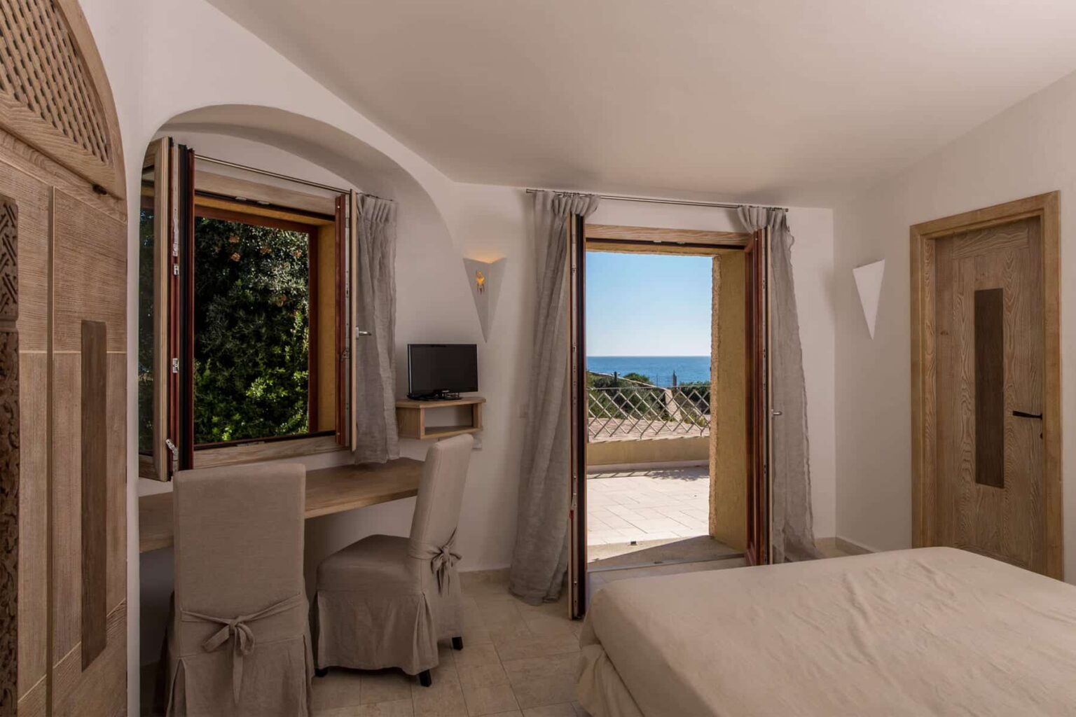 Cozy bedroom with a desk and chair, featuring a large window that opens to a stunning sea view. Light-colored curtains and neutral decor create a serene atmosphere, ideal for relaxation and work. | Only on SopranoVillas