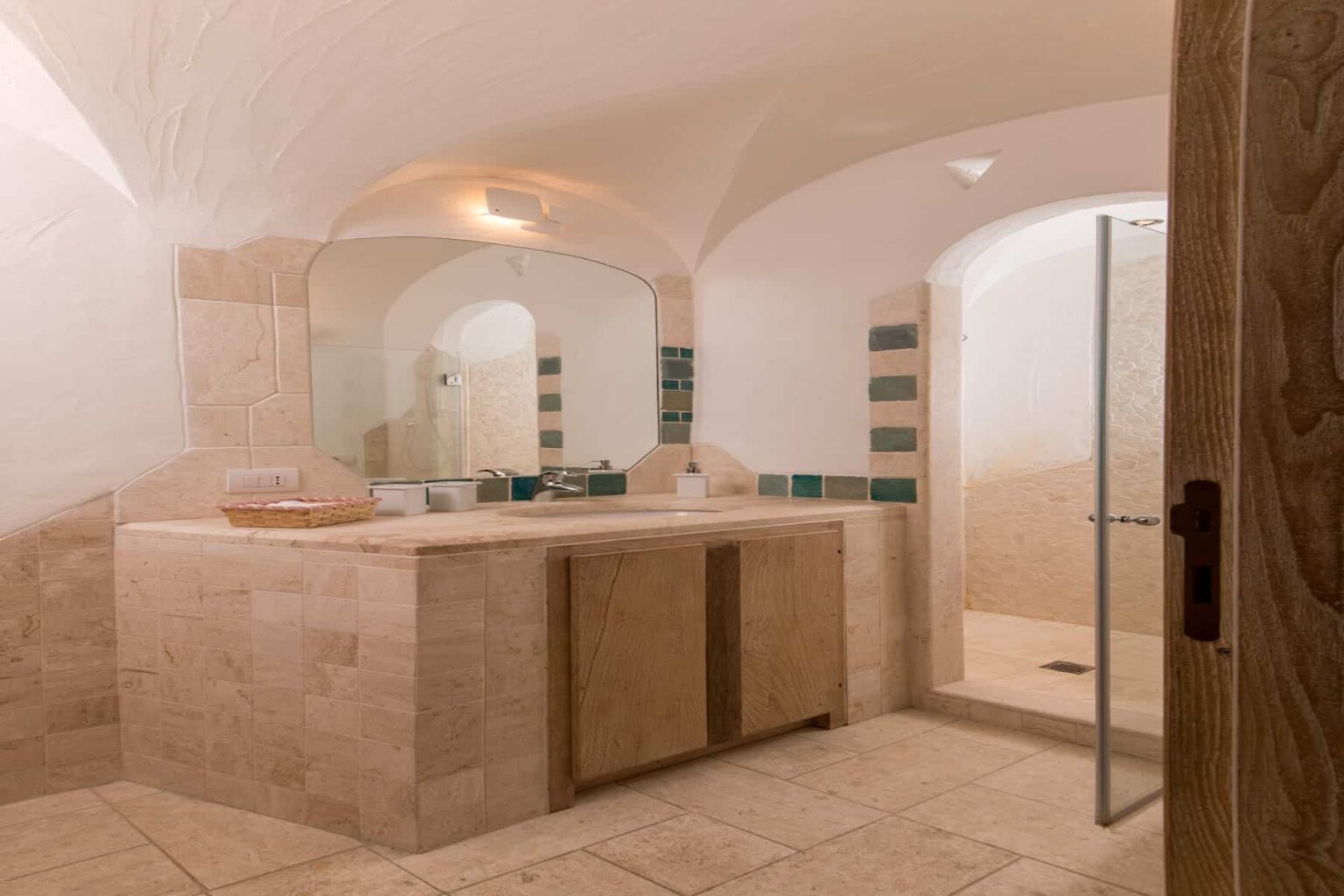 Spacious modern bathroom with arched ceilings, featuring a double sink vanity, large mirror, and a glass shower enclosure, complemented by elegant tile work and warm lighting. | Only on SopranoVillas