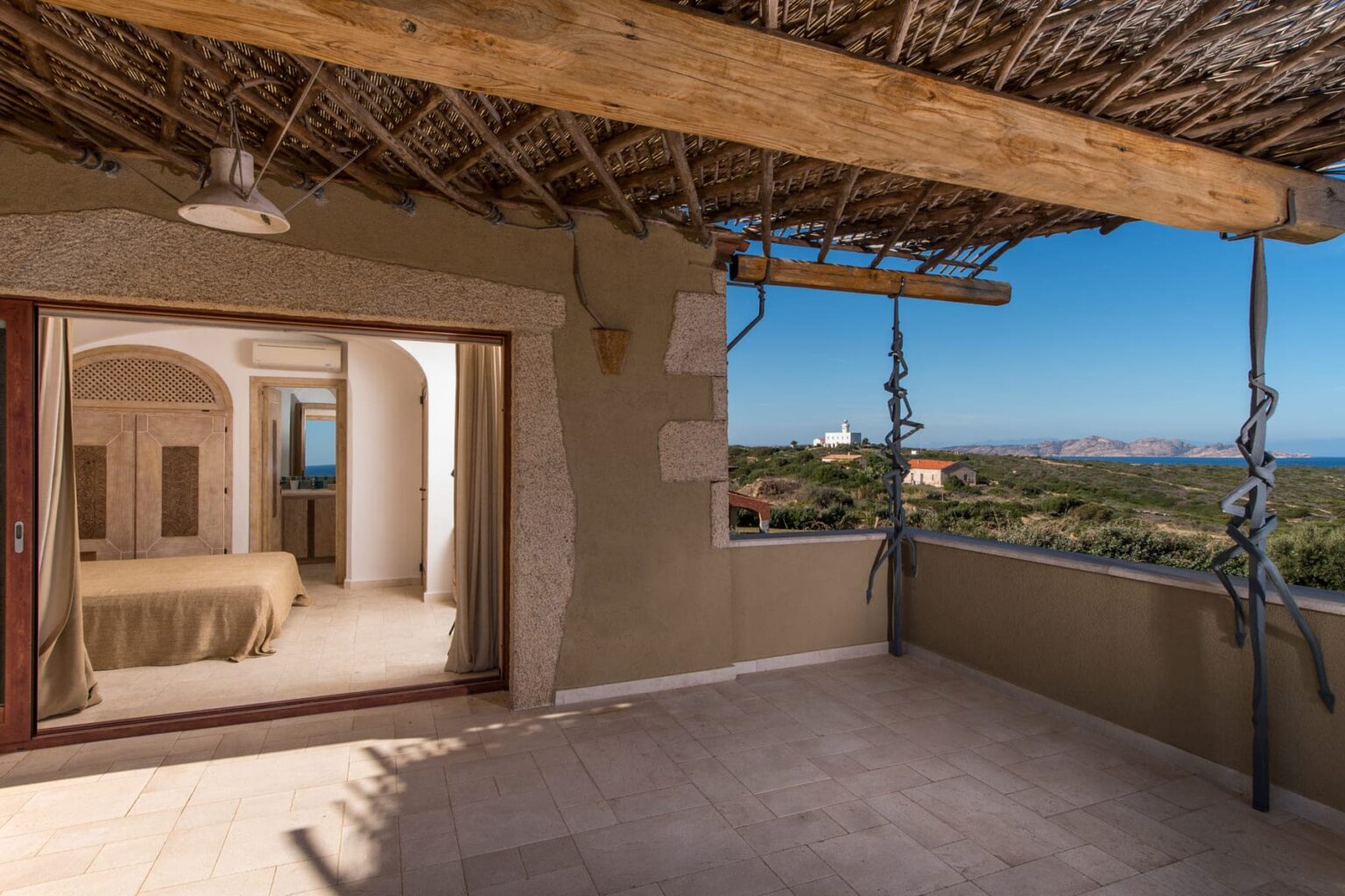 Spacious balcony with a stunning ocean view, featuring rustic decor and an adjoining bedroom with a cozy bed, perfect for relaxation and enjoying nature. | Only on SopranoVillas