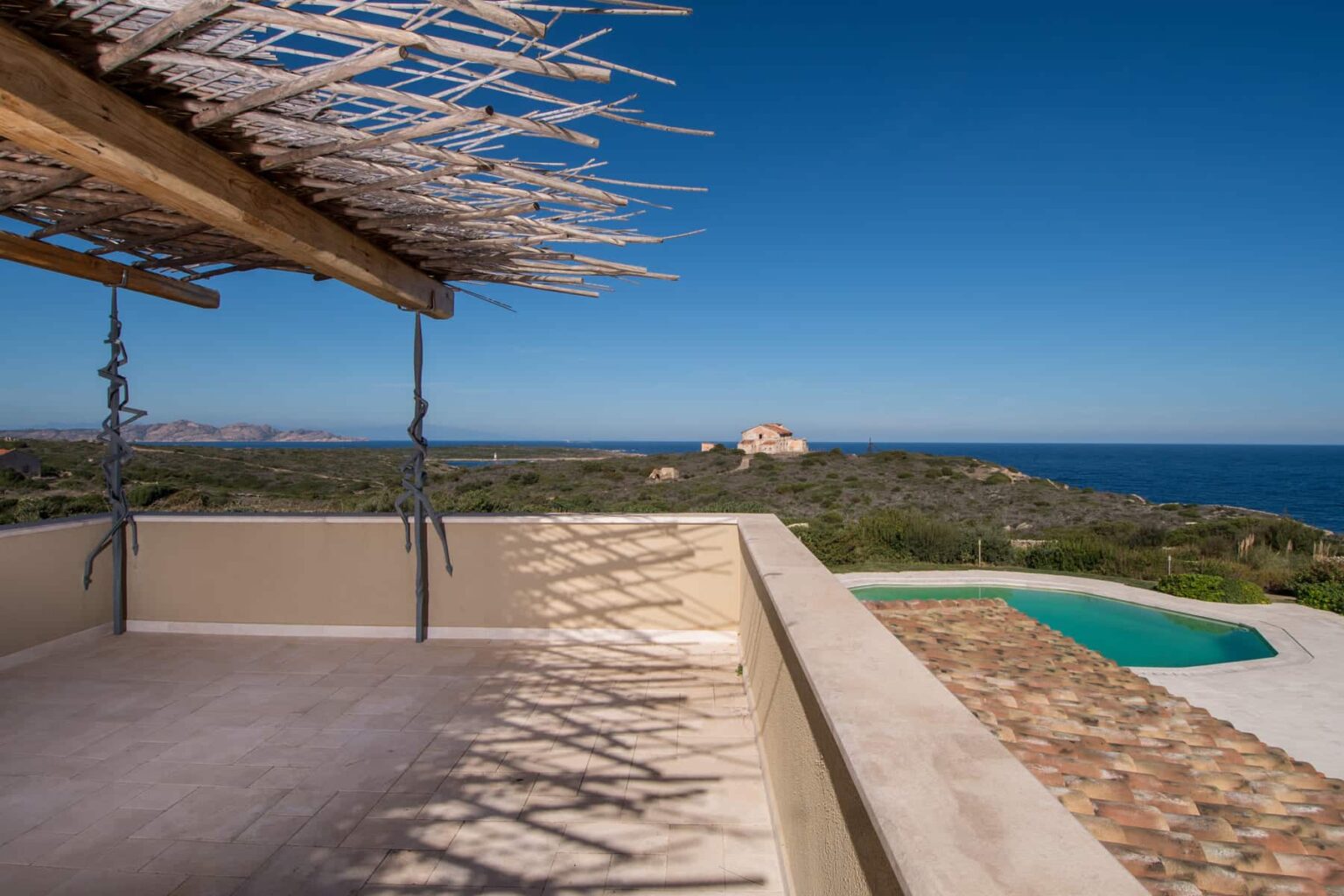 Scenic ocean view from a terrace with a shaded seating area and a private pool, showcasing a serene landscape and clear blue skies. | Only on SopranoVillas