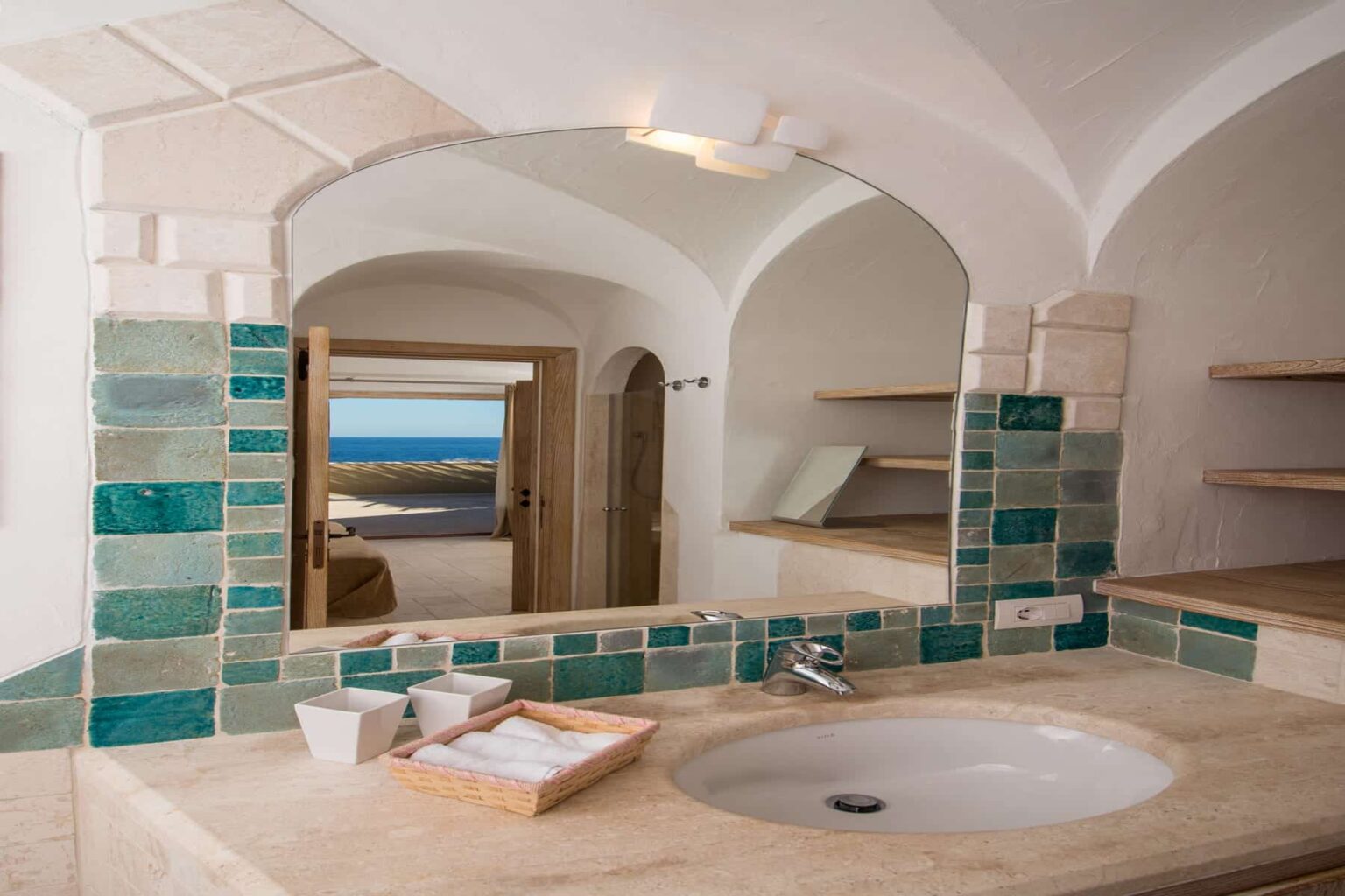Modern bathroom interior featuring arched ceilings, green and beige tiled accents, a circular sink, and a view of the ocean through an open door. Ideal for showcasing luxury accommodations or interior design inspiration. | Only on SopranoVillas