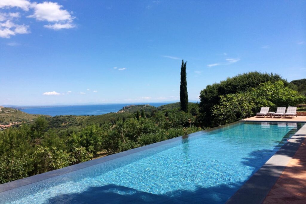Stunning infinity pool overlooking a lush green landscape and the ocean under a clear blue sky, perfect for luxury vacation rentals or serene retreats. | Only on SopranoVillas