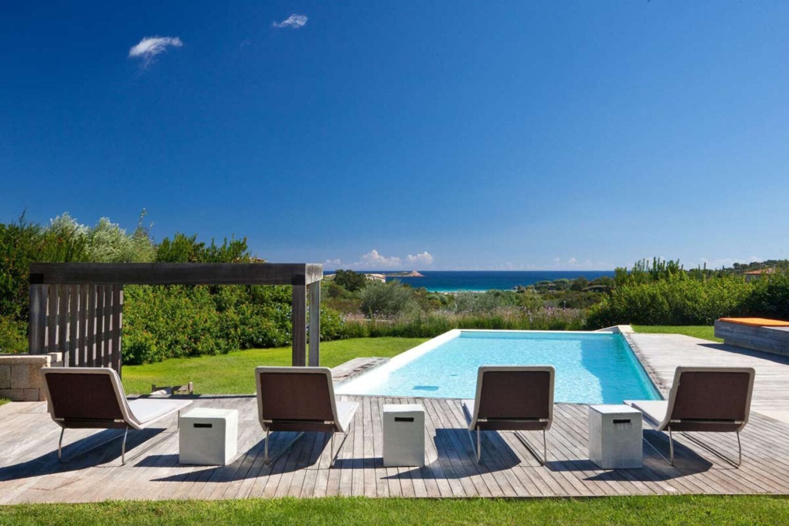 Modern outdoor pool area with lounge chairs and ocean view under a clear blue sky. | Only on SopranoVillas