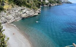 Scenic view of a secluded beach in Italy, showcasing crystal-clear turquoise waters and rocky cliffs, ideal for luxury villa rentals.